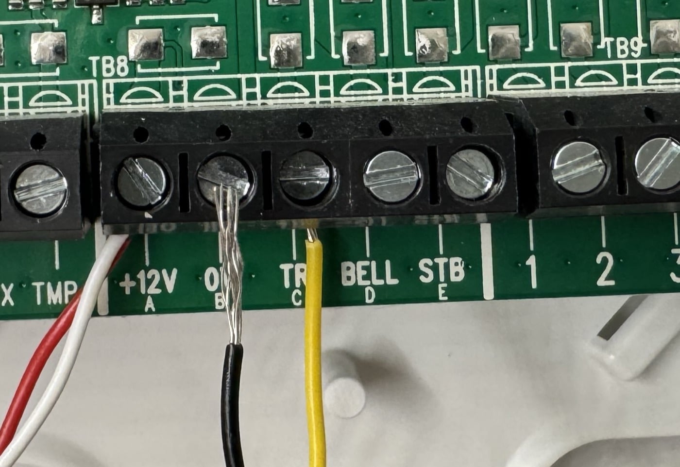 Legacy alarm panel terminal strip labeled +12V, 0V, TR, BELL, and STB